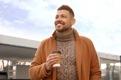 Man with cup of coffee on city street in morning