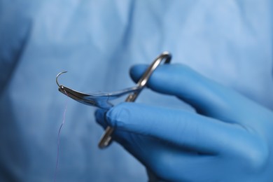 Photo of Professional surgeon holding forceps with suture thread, closeup. Medical equipment