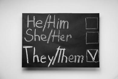 Gender equality. Small blackboard with written pronouns on beige background, top view