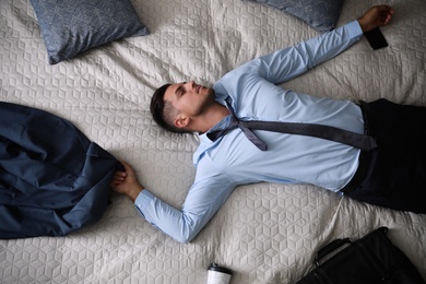 Exhausted businessman in office wear sleeping on bed at home after work, top view