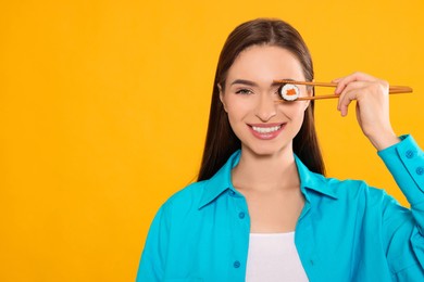 Photo of Funny young woman holding sushi roll with chopsticks on orange background. Space for text