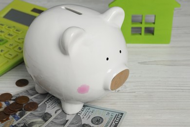 Photo of Piggy bank, house model, calculator and money on white wooden table, closeup. Space for text