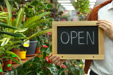 Male business owner holding OPEN sign in his flower shop, closeup