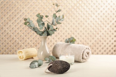 Photo of Pumice stone, candle, towel and eucalyptus on white wooden table