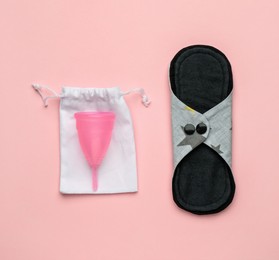 Reusable cloth pad and menstrual cup on pink background, flat lay