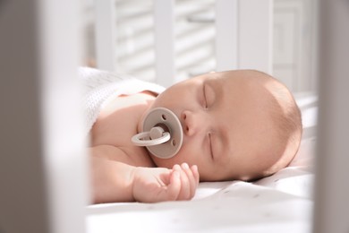 Cute little baby with pacifier sleeping in crib at home