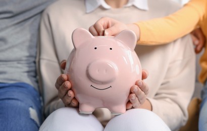 Photo of Family putting coin into piggy bank at home, closeup
