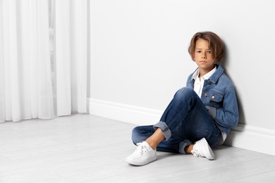 Cute little boy in casual outfit near white wall in room. Space for text