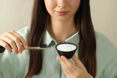 Photo of Young woman with toothbrush and bowl of baking soda on beige background, closeup