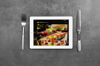 Modern tablet with open page for online food ordering and cutlery on black table, flat lay. Concept of delivery service