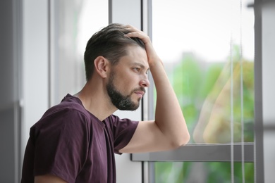Lonely depressed man near window at home