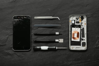 Damaged smartphone and repair tools on black background, flat lay
