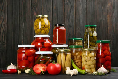 Glass jars with different pickled vegetables and mushrooms on wooden background