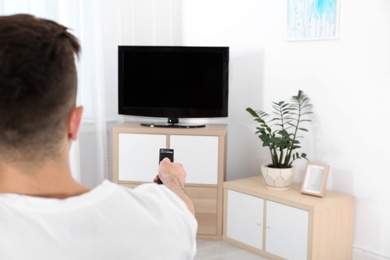 Young man switching channels on modern TV with remote control at home