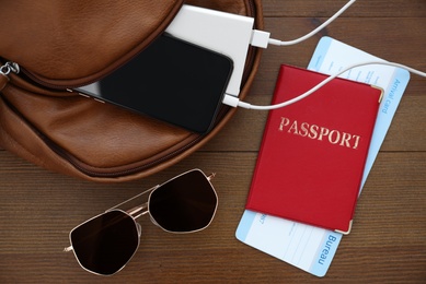 Sunglasses, passport and backpack with gadgets on wooden table, flat lay