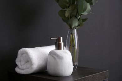 Clean soft towel and soap dispenser on stand near black wall