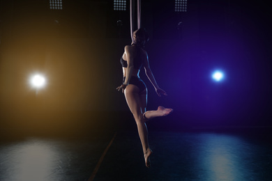 Young woman performing acrobatic element on aerial silk indoors