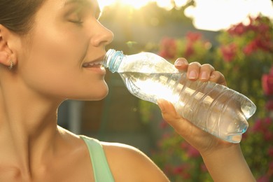 Happy young woman drinking water outdoors on hot summer day, closeup. Refreshing drink
