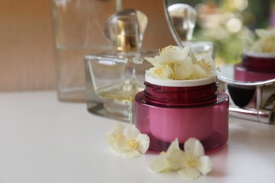 Jar of cream with beautiful jasmine flowers, perfume and mirror on white table, closeup. Space for text