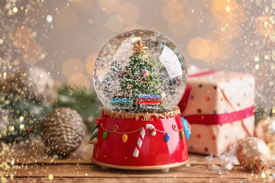 Beautiful snow globe with Christmas tree on wooden table. Bokeh effect