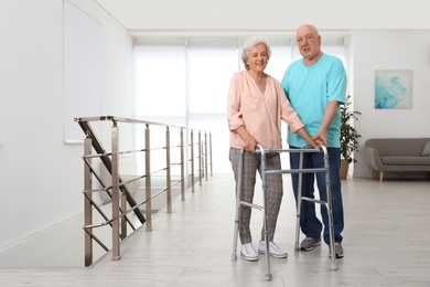 Elderly man helping his wife with walking frame indoors