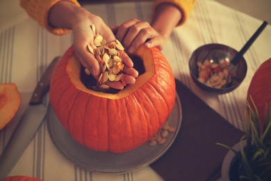 Woman making pumpkin jack o'lantern at table, closeup. Halloween celebration