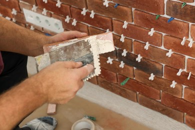 Professional builder applying cement onto decorative brick near wall, closeup. Tiles installation process