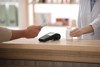 Customer using terminal for contactless payment with smartphone in pharmacy, closeup