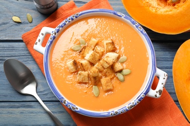 Tasty creamy pumpkin soup with croutons and seeds in bowl on blue wooden table, flat lay