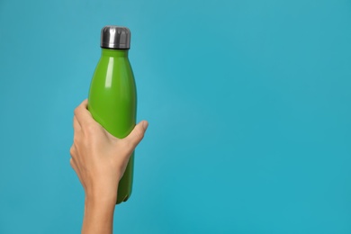 Woman holding modern green thermos on light blue background, closeup. Space for text