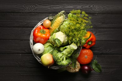 Photo of Different fresh vegetables in wicker basket on black wooden table, top view. Farmer harvesting