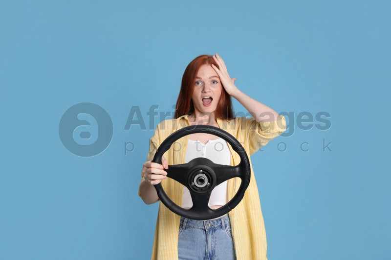 Emotional young woman with steering wheel on light blue background