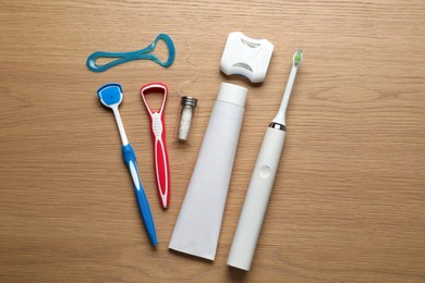 Flat lay composition with tongue cleaners and teeth care products on wooden table