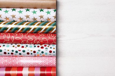 Different colorful wrapping paper rolls on white wooden table, flat lay. Space for text