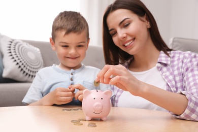 Happy mother and son putting coins into piggy bank at home
