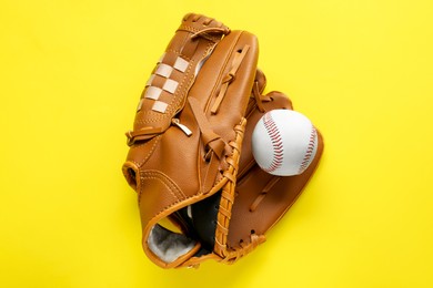 Photo of Catcher's mitt and baseball ball on yellow background, top view. Sports game