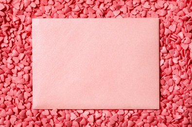 Blank card on pile of pink heart shaped sprinkles, top view. Space for text