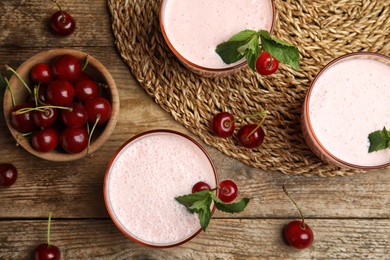 Tasty fresh milk shakes with cherries on wooden table, flat lay