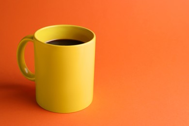 Yellow mug of freshly brewed hot coffee on orange background, space for text