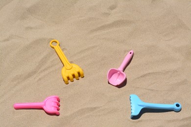 Photo of Bright plastic rakes and shovels on sand. Beach toys