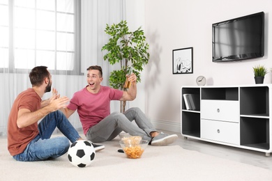 Young men watching TV while sitting on floor at home. Sport channel