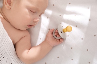 Cute little baby with pacifier sleeping in bed, top view