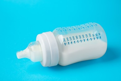 Photo of One feeding bottle with milk on light blue background, closeup