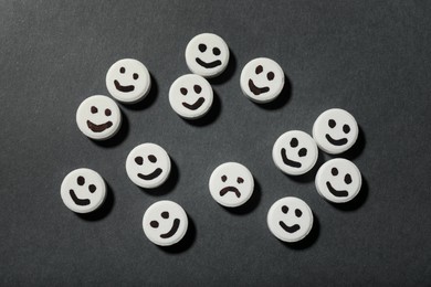 Pill with sad face among happy ones on black background, flat lay. Depression concept