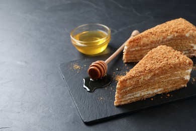 Slices of delicious layered honey cake served on black table. Space for text