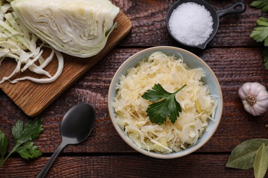 Photo of Bowl of tasty sauerkraut and ingredients on wooden table, flat lay