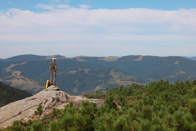 Man with backpack on rocky peak in mountains, back view