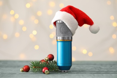 Microphone with Santa hat and festive decor on blue wooden table against blurred lights. Christmas music