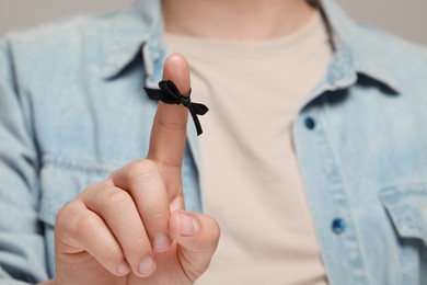 Photo of Man showing index finger with tied bow as reminder against light grey background, focus on hand