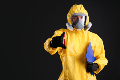 Man in chemical protective suit holding test tube of blood sample on black background, space for text. Virus research